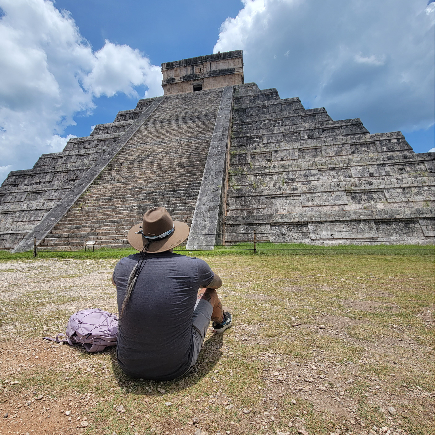 David Barazarte sitting down on grounf facing pyramid in Mexico reflecting on it's grandeur